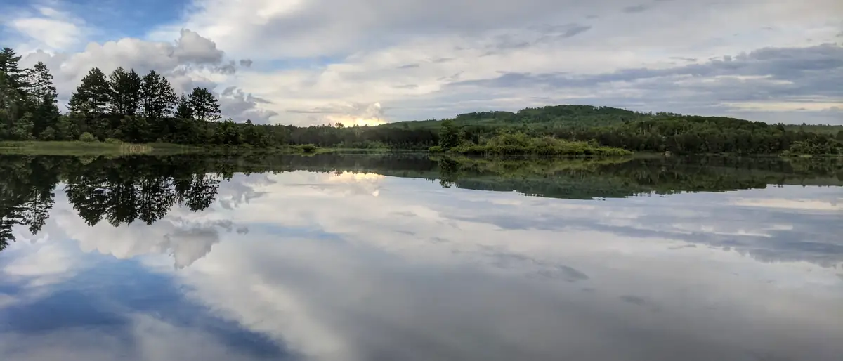 A still lake in northern Minnesota after a June storm, a green treeline and a wide cloudy sky mirrored in the water.